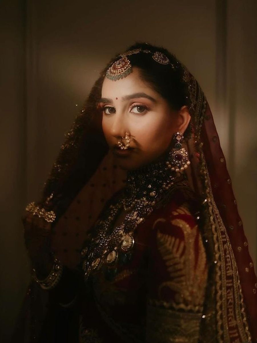 A bride in a deep maroon and gold lehenga with traditional jewellery